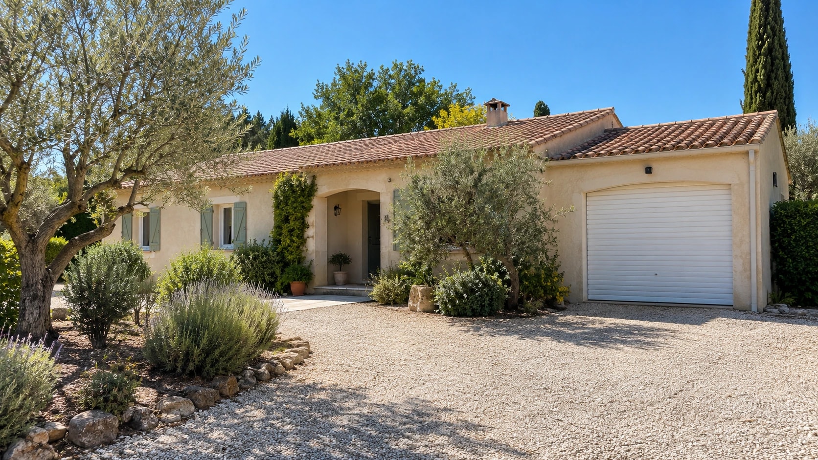 Porte de garage enroulable blanche sur une maison provençale de plain-pied, entre les oliviers